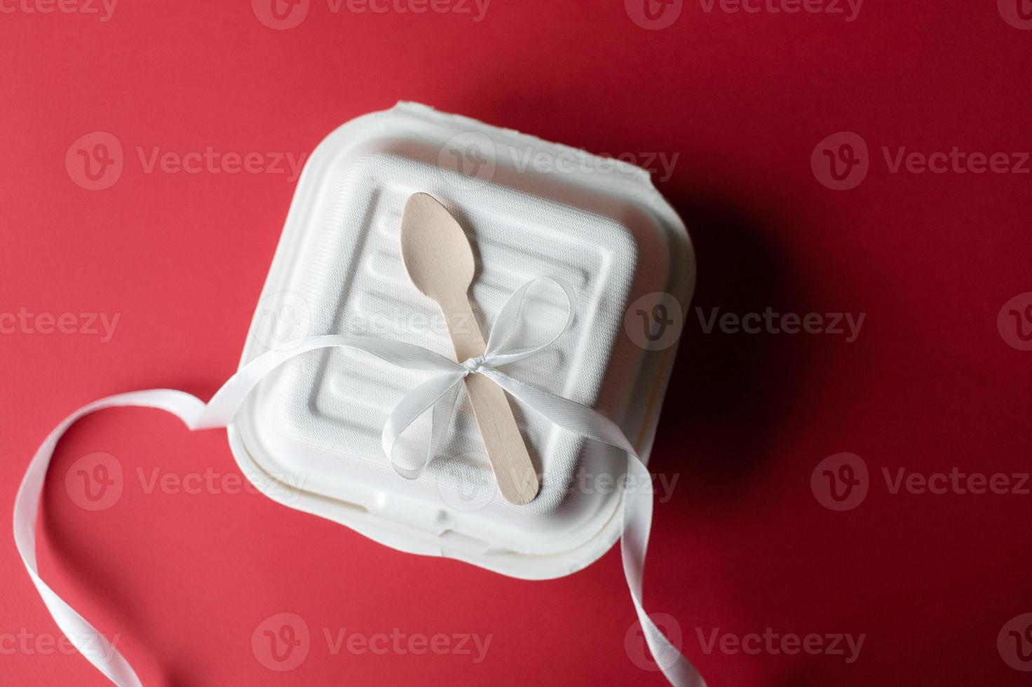 A closed bento cake box with a wooden spoon on a red background. Ribbon for gifts photo