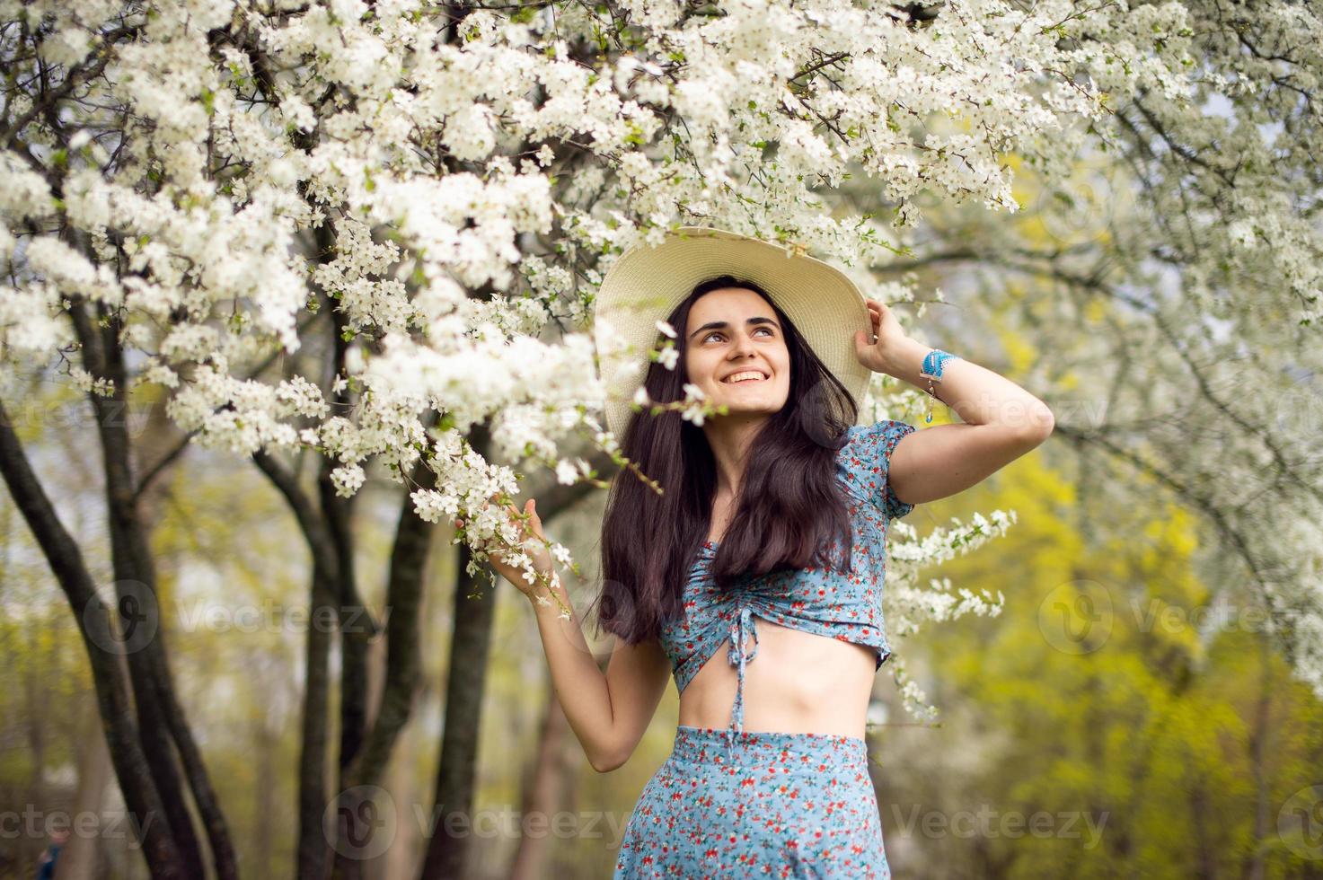 un joven niña en un sombrero y con tulipanes, en pie en un azul vestir siguiente a un floreciente blanco árbol. foto