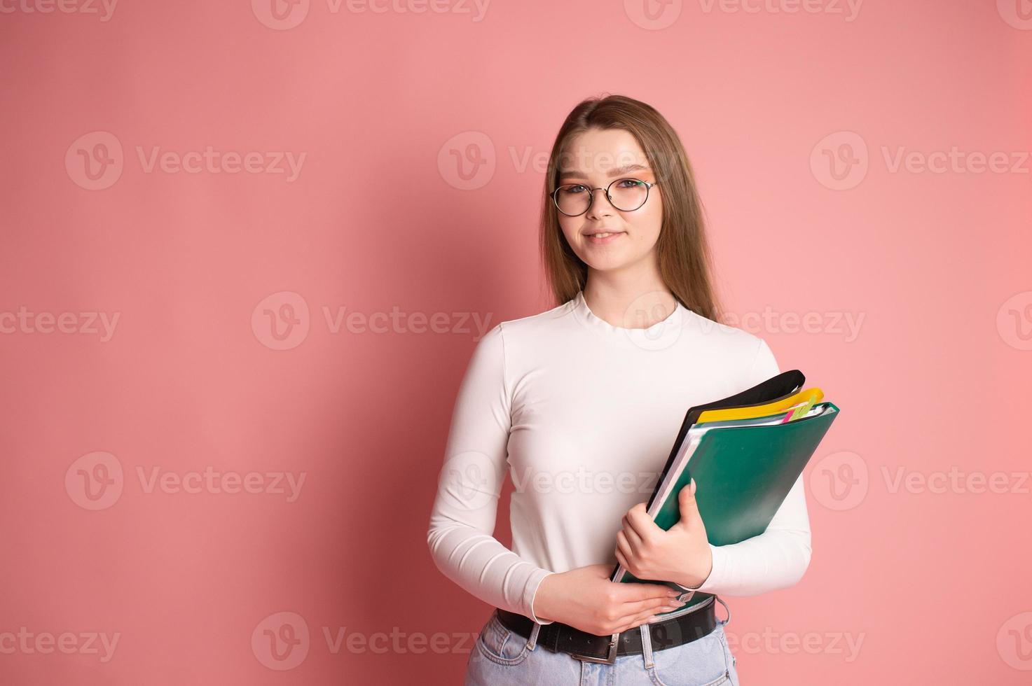 Cute student with glasses holds colorful folders on a pink background photo