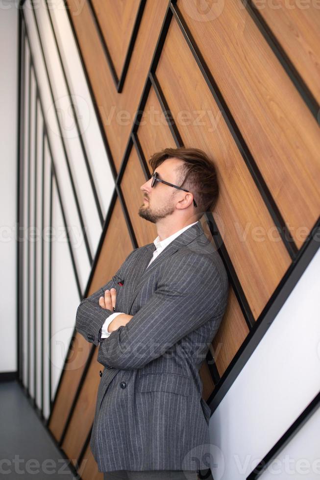a young man in a suit and sunglasses is standing in a room near the wall photo