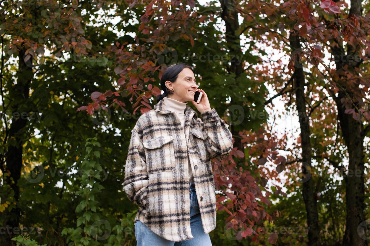 A cute girl has a pleasant conversation on the phone against the background of an autumn forest photo