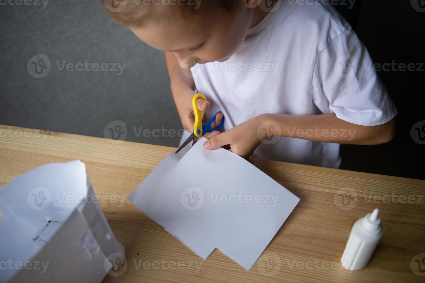 The boy cuts out details from paper. Glue the parts together with glue photo
