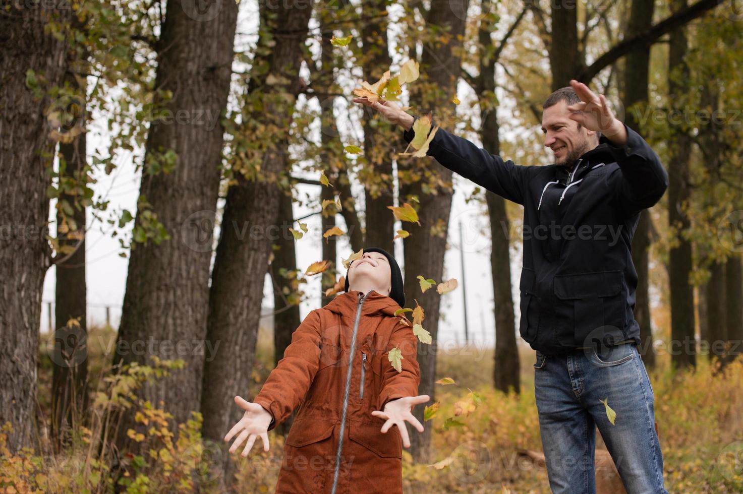 Dad throws autumn yellow leaves on his son and laughs photo