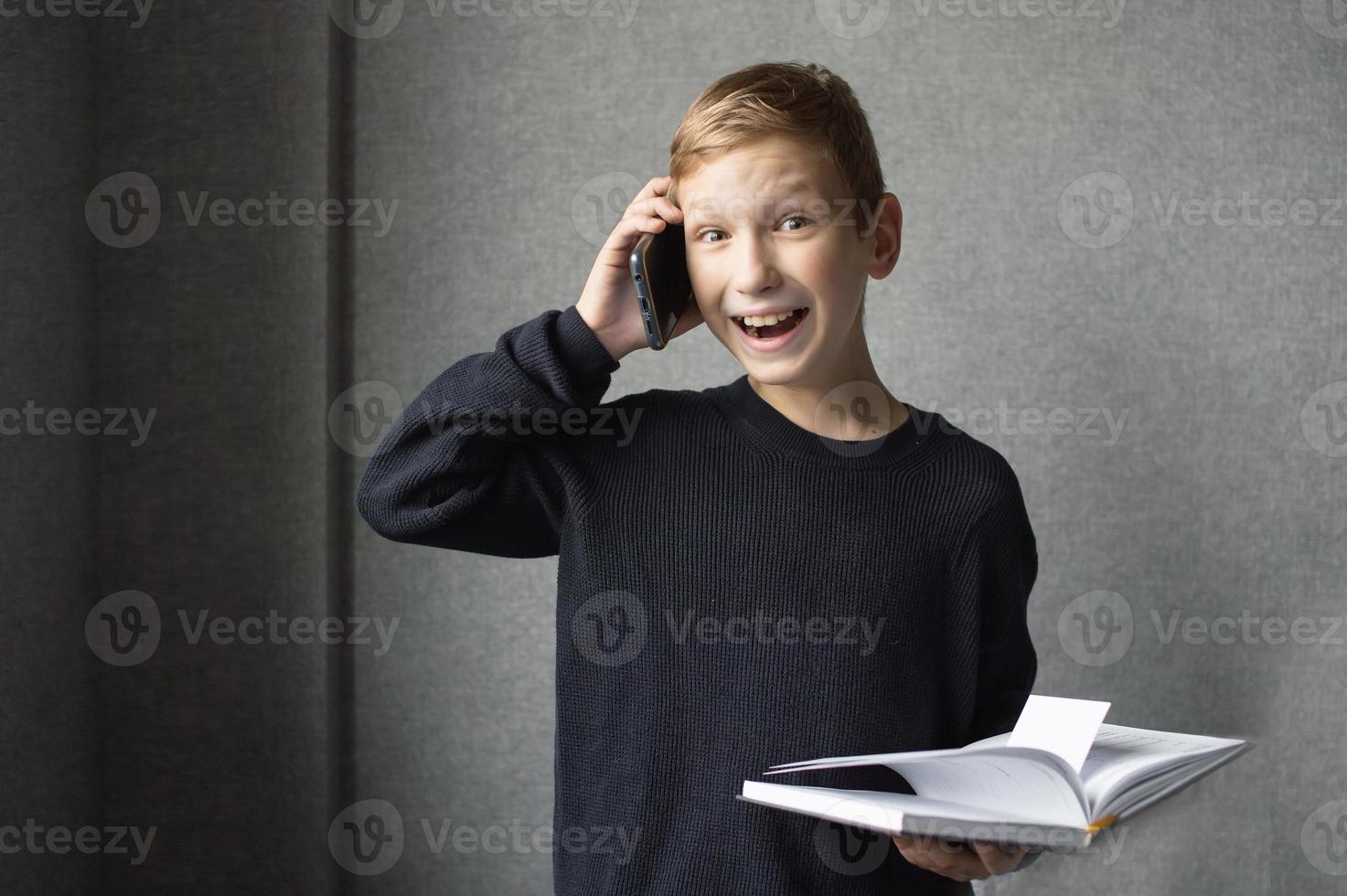 A happy boy is holding a book in his hands and talking on the phone photo