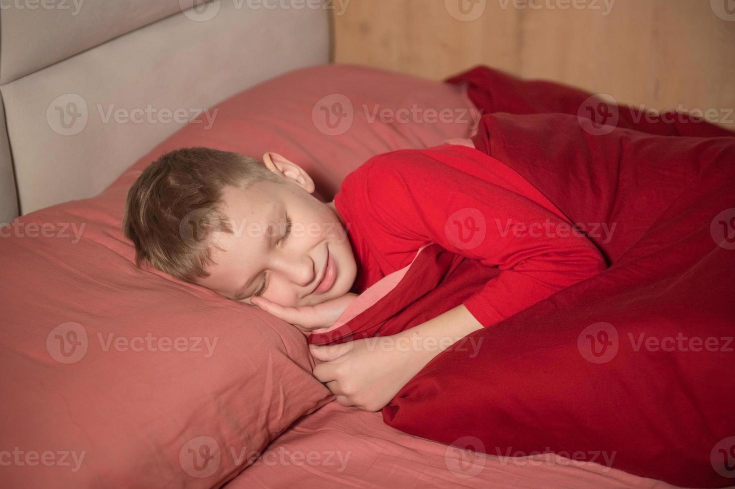 Cute boy in red pajamas sleeping with his eyes closed in bed and smiling photo