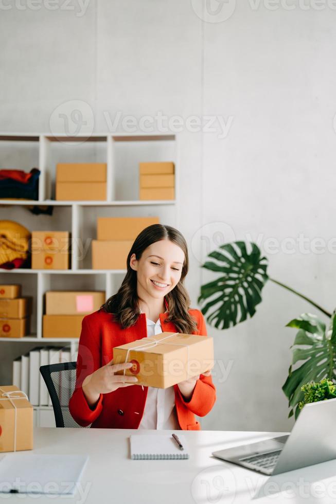 Startup small business SME, Entrepreneur owner woman using smartphone or tablet taking receive and checking online purchase shopping order to preparing pack product box. photo