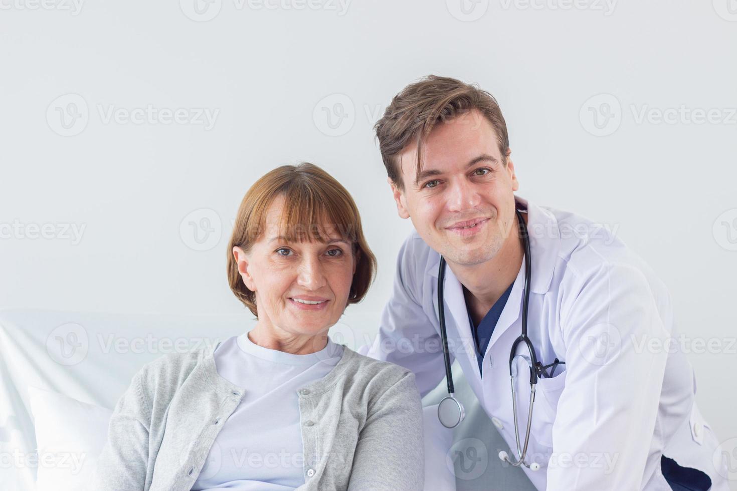 the doctor is examining the patient in the hospital. Caucasian doctor wearing gown and listening device and a female patient looking at the camera at the hospital photo