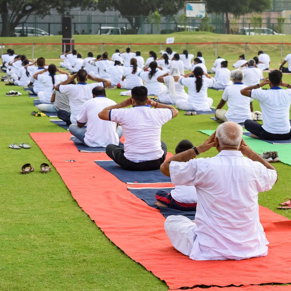 New Delhi, India, June 21 2022 - Group Yoga exercise session for people at Yamuna Sports Complex in Delhi on International Yoga Day, Big group of adults attending yoga class in cricket stadium photo