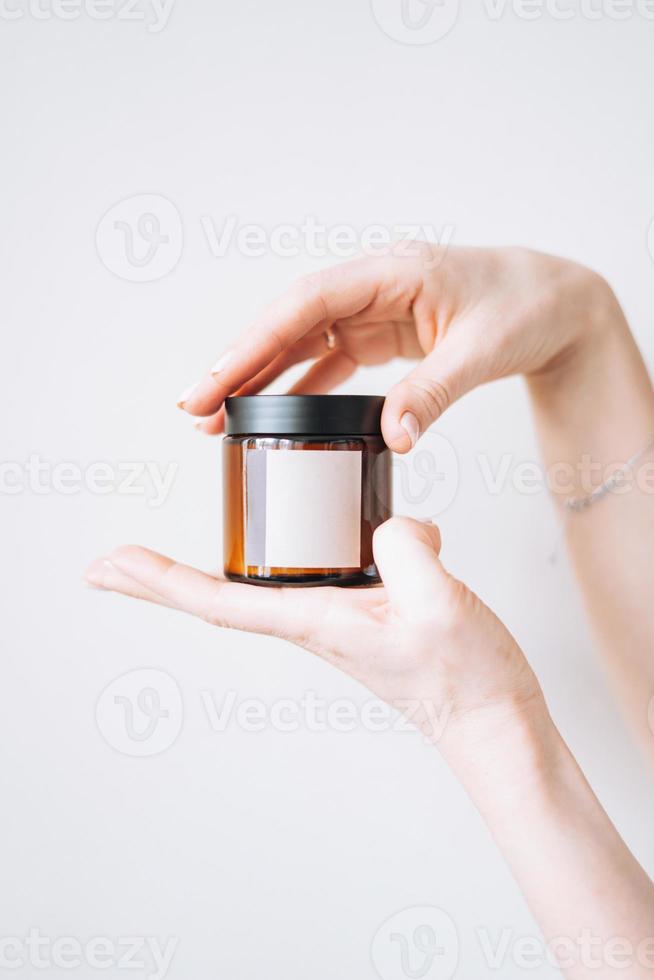 Women's hands hold glass jar with empty label on light background, mockup photo