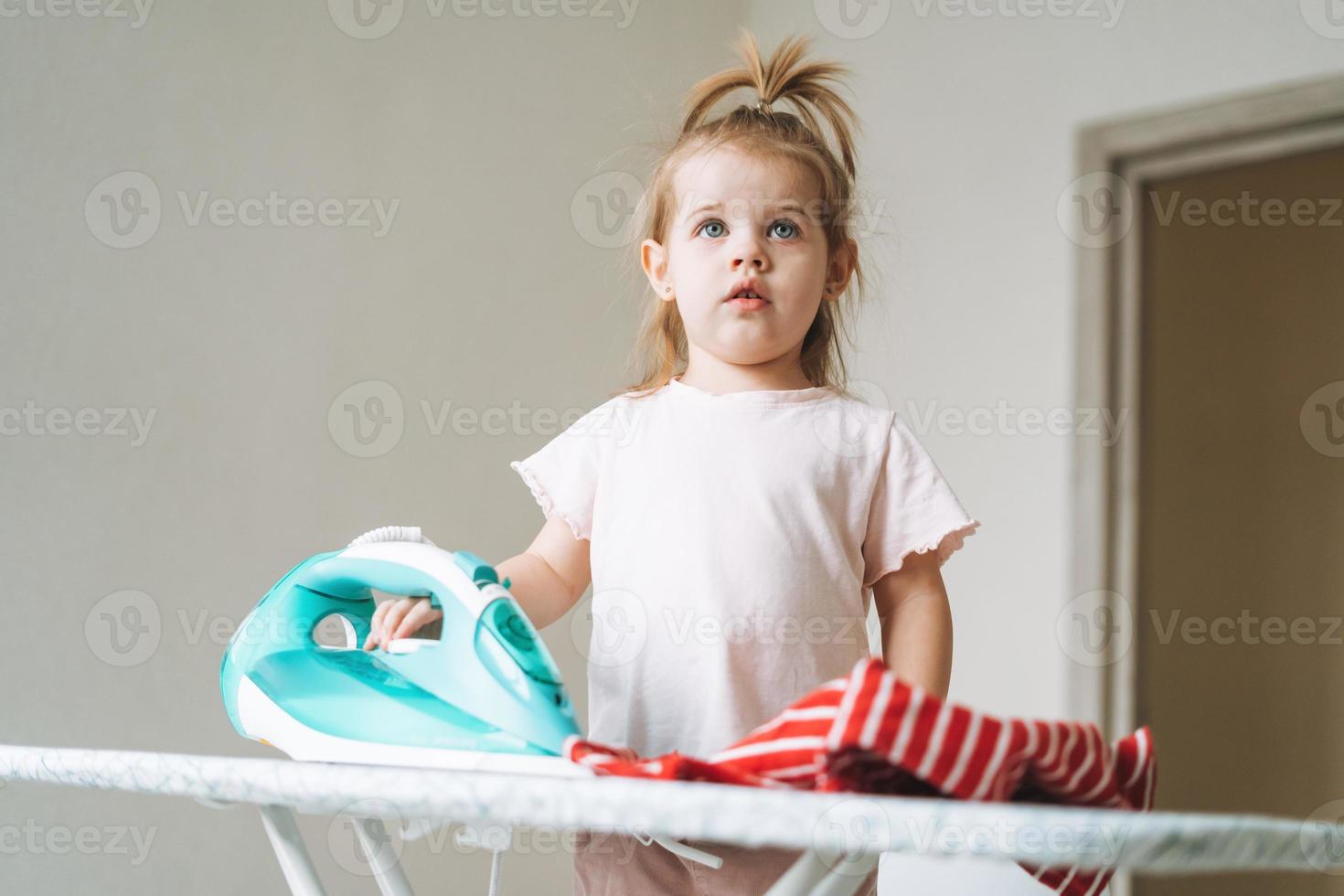 Cute little baby girl playing and ironing clothes with an iron at home photo