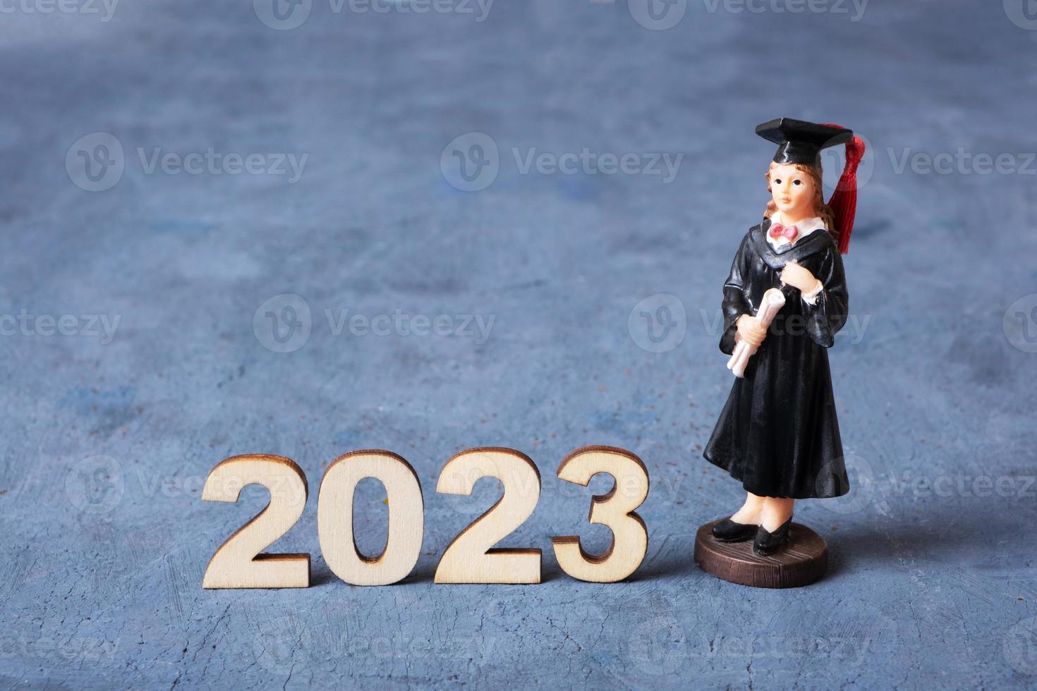 Class of 2023 concept. Wooden number 2023 with graduate statuette on concrete background photo