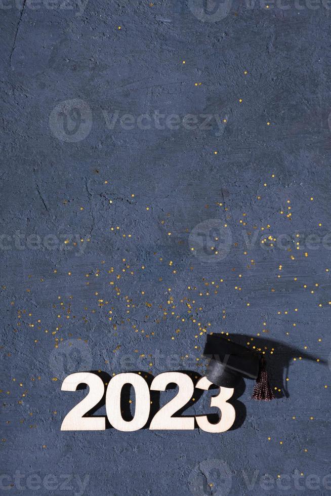 Class of 2023 concept. Wooden number 2023 with graduate statuette on concrete background with tinsel top view photo