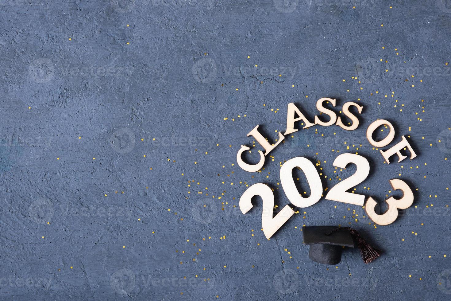 Class of 2023 concept. Wooden number 2023 with graduate statuette on concrete background with tinsel top view photo