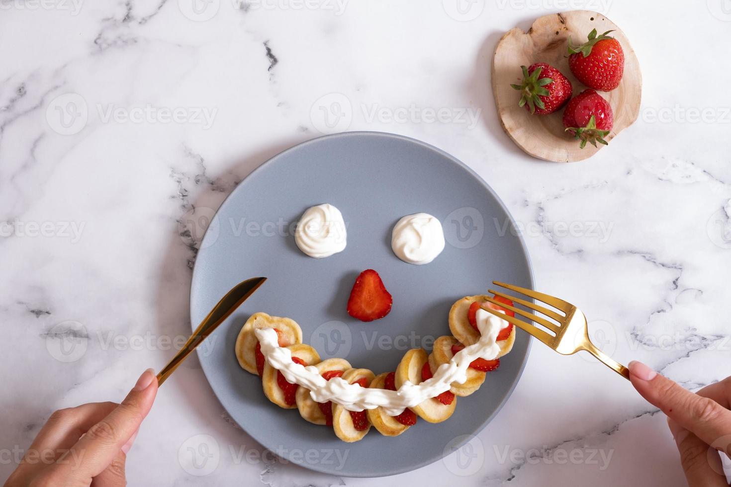 Small pancakes with strawberries in the original serving in the form of a smiley face. Top view. Flat lay photo