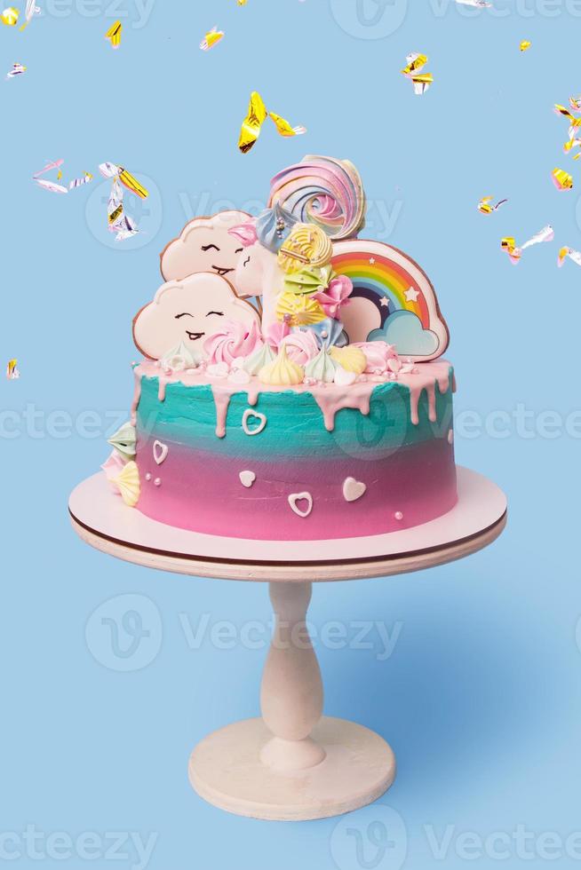 Beautiful festive children's cake with a unicorn on a stand on a blue background with falling golden confetti photo