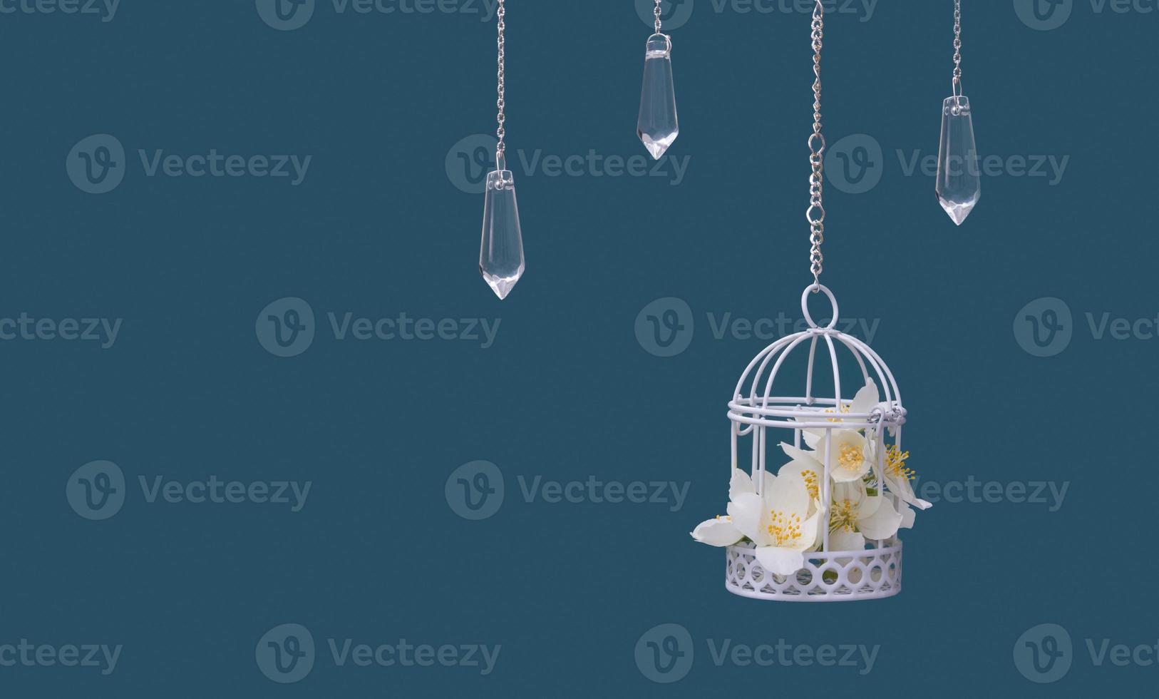 Decorative cage with jasmine flowers and glass pendants on chains on a turquoise background. Beautiful festive wedding concept photo