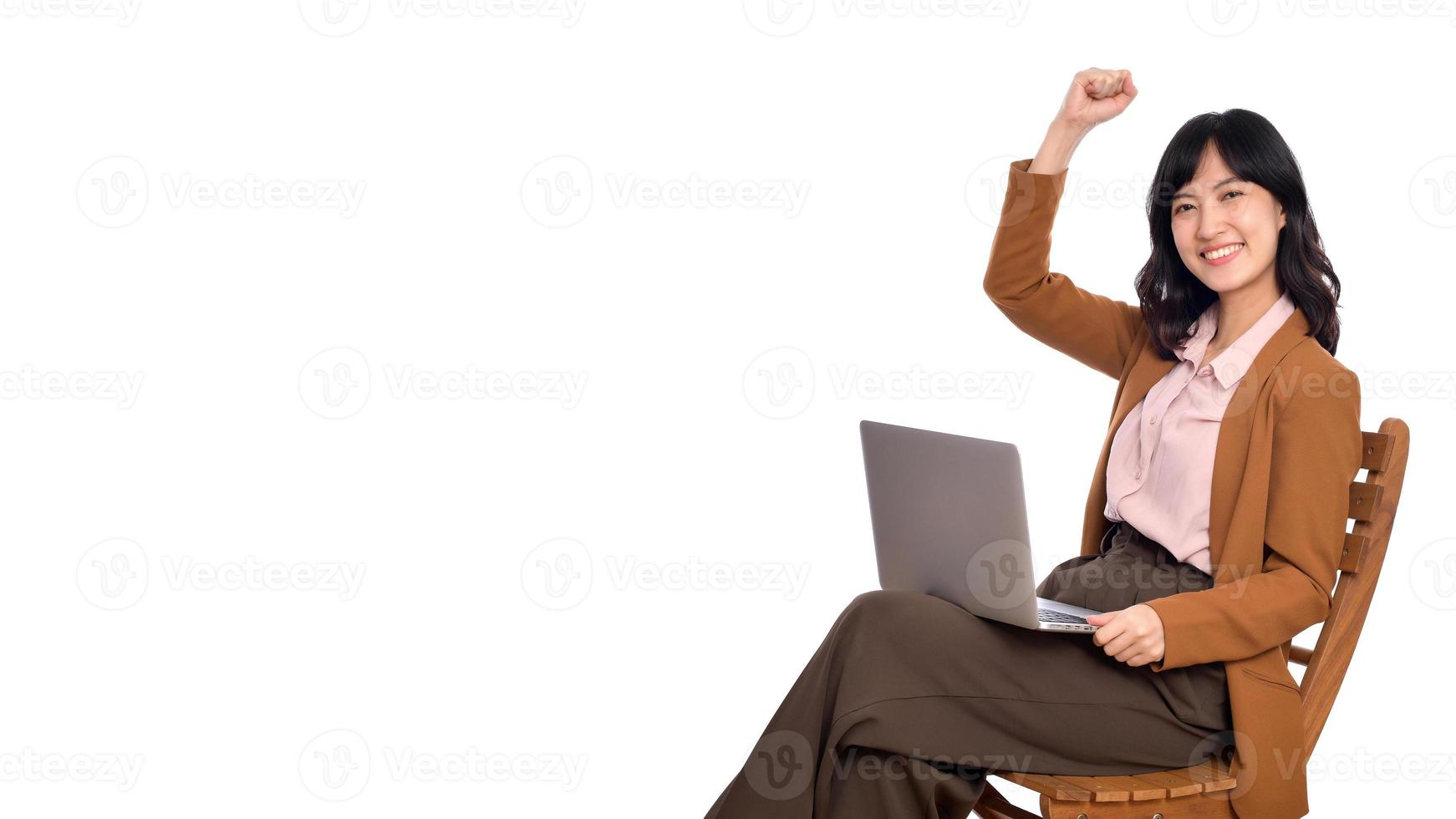 Happy young business asian woman celebrating on her success. While her using laptop sitting on wooden chair isolate on white background photo