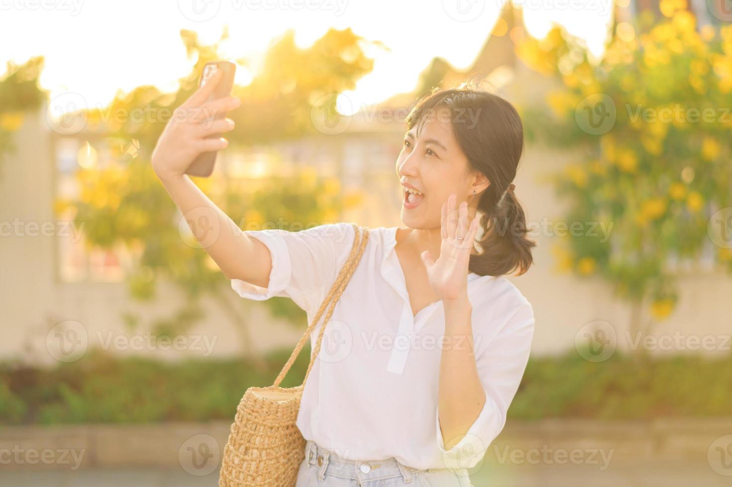 retrato joven hermosa asiático mujer utilizando teléfono inteligente a vídeo llamada con amigo y explorar calle en verano vacaciones en bangkok, Tailandia foto