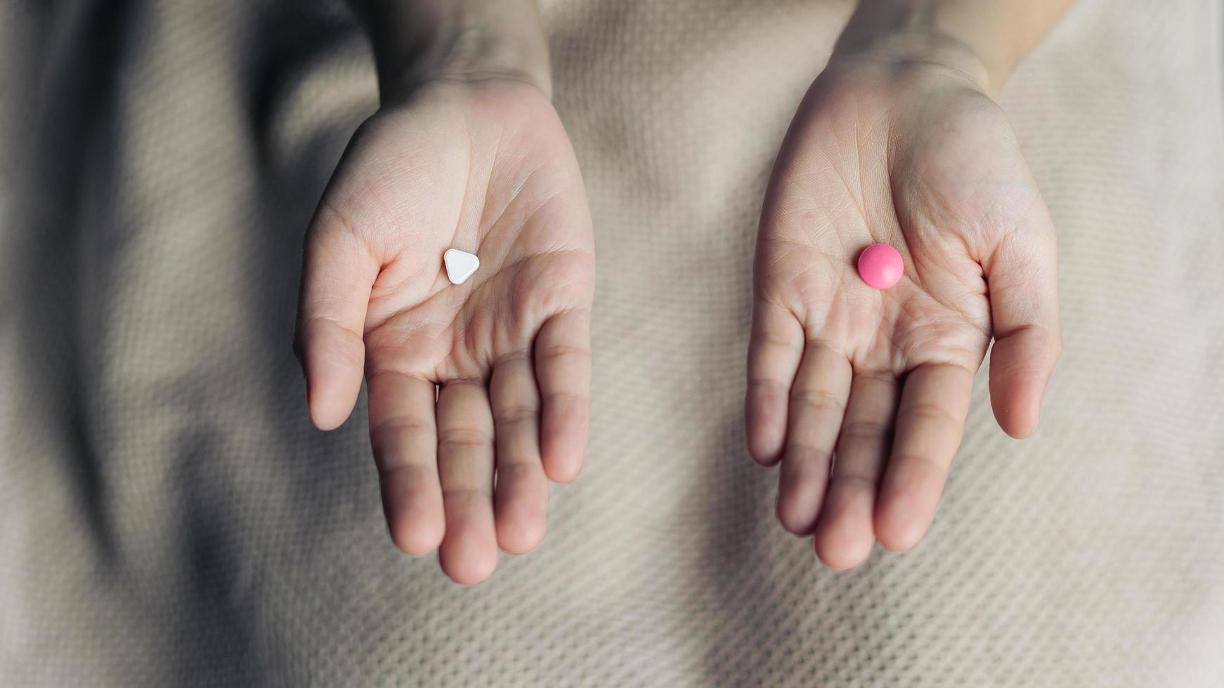 Female hands hold and offer two choice medicine pills capsule for chosen. White and pink candy or meds compare to choose from. Concept decision making or indecisiveness. photo