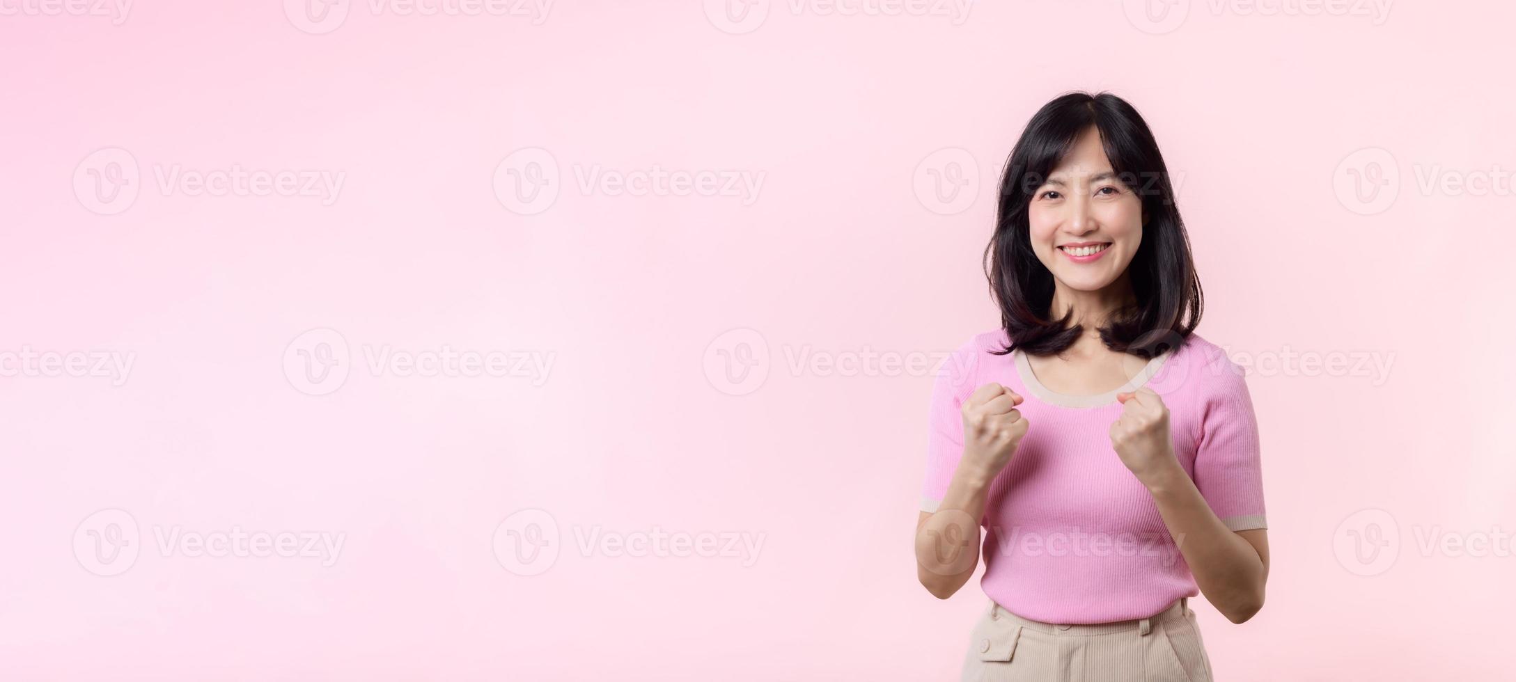 Portrait beautiful young asian woman happy smile with fist up victory gesture expression cheerful her success achievement against pink pastel studio background. Woman day winner celebration concept. photo