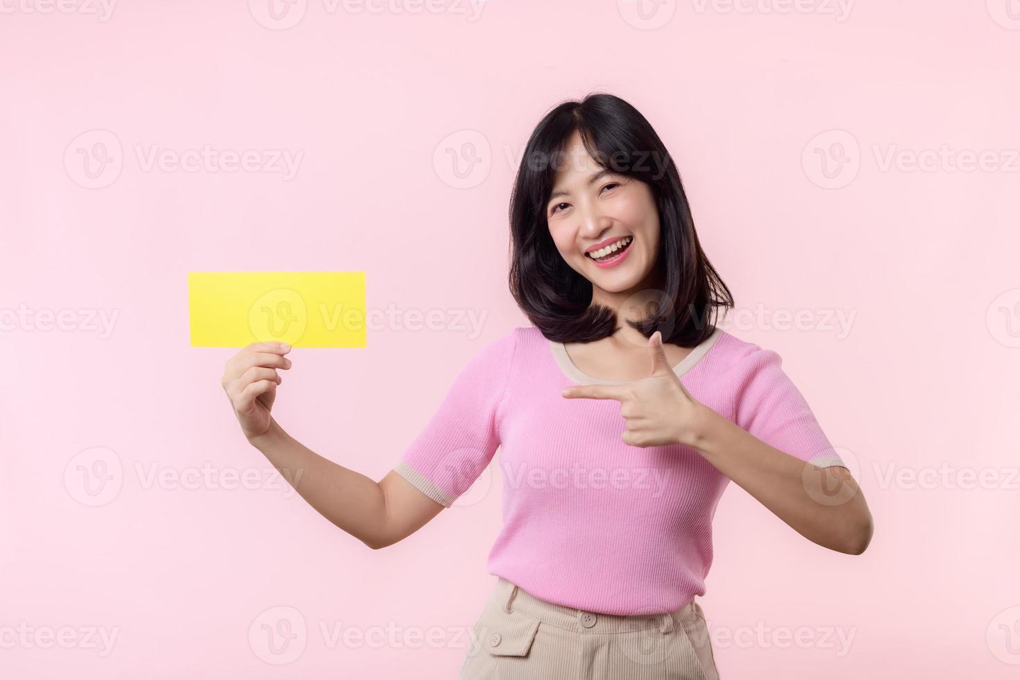 Portrait happy young woman model holding and showing blank space paper for advertisement information message poster with thumb up or point finger gesture isolated on pink pastel studio background. photo