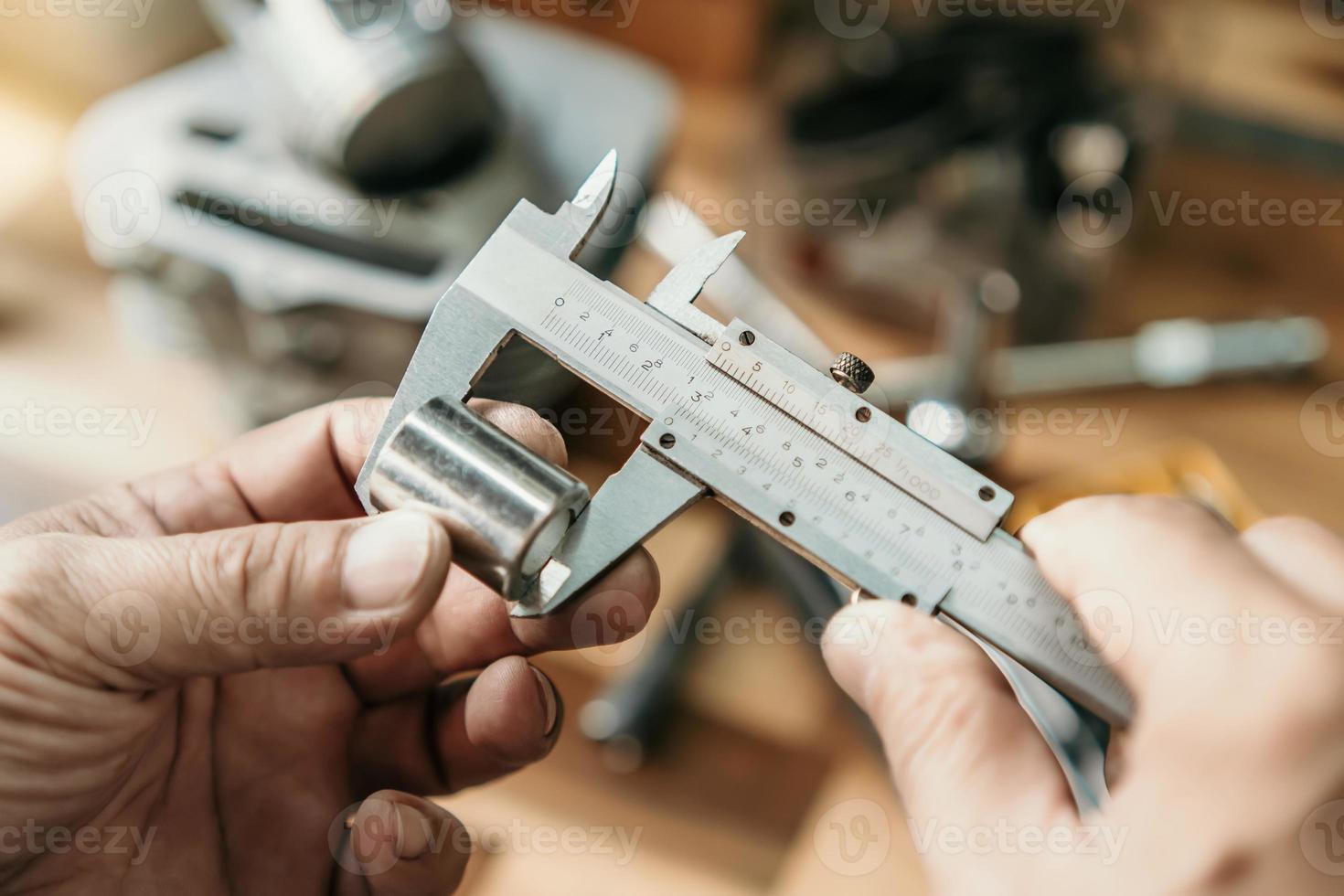 Hand of mechanic holding Vernier Caliper Measurements on a steel Shaft Bush or motorcycle part at motorcycle shop , selective focus, photo