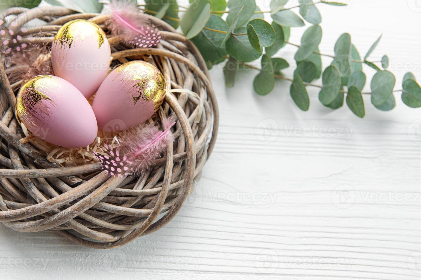 Easter eggs painted pink and gold and  feathers in a nest on a white wooden background. photo