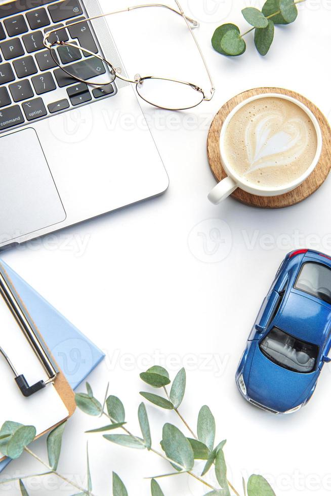 Modern white office desk table with laptop, notebook, toy car and other supplies. photo