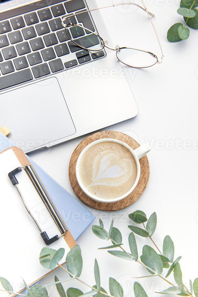 Modern white office desk table with laptop, notebook and other supplies. photo