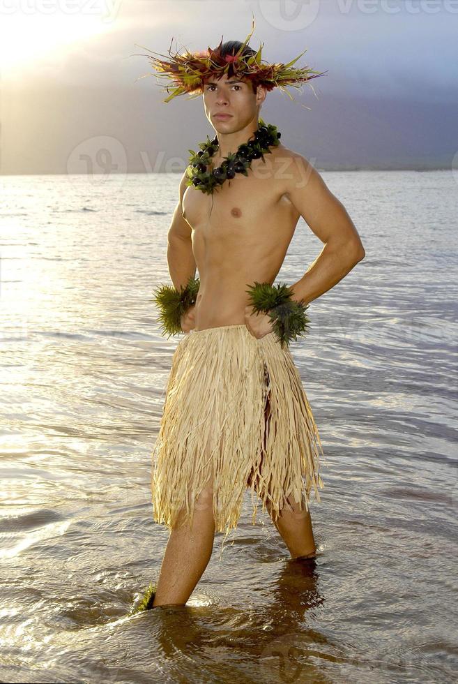 Handsome male hula dancer stands in the water as the sun sets. photo