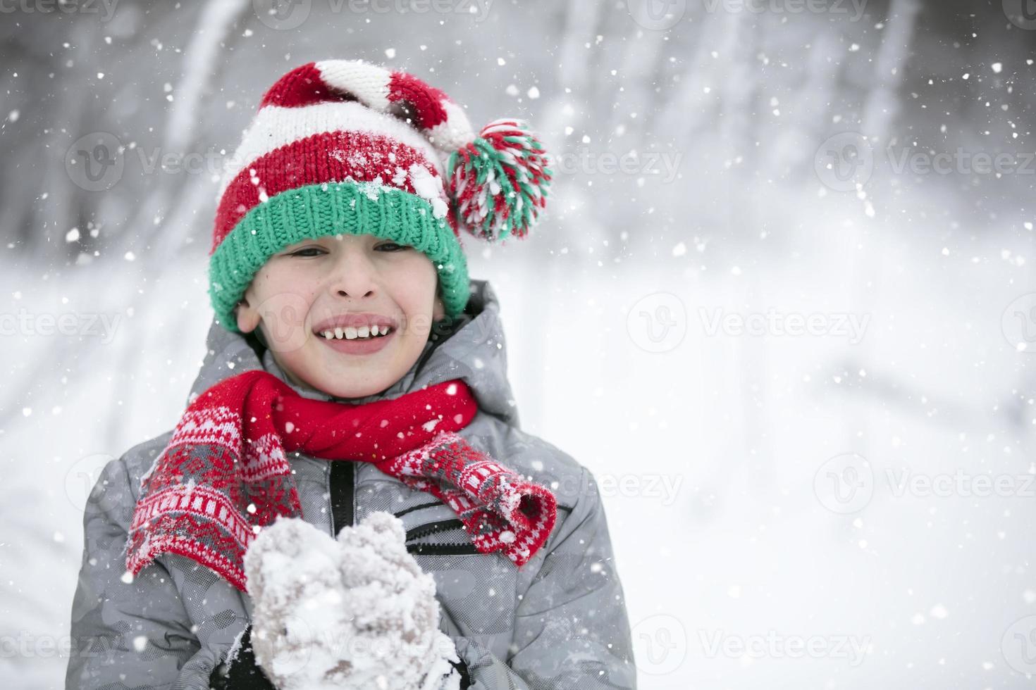 contento chico en un invierno día mira a el cámara, sonrisas un niño obras de teatro en el invierno con nieve. foto