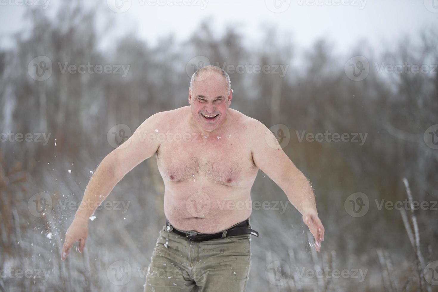 An adult man is hardened by snow on a winter day. Man with snow showers to harden his body photo