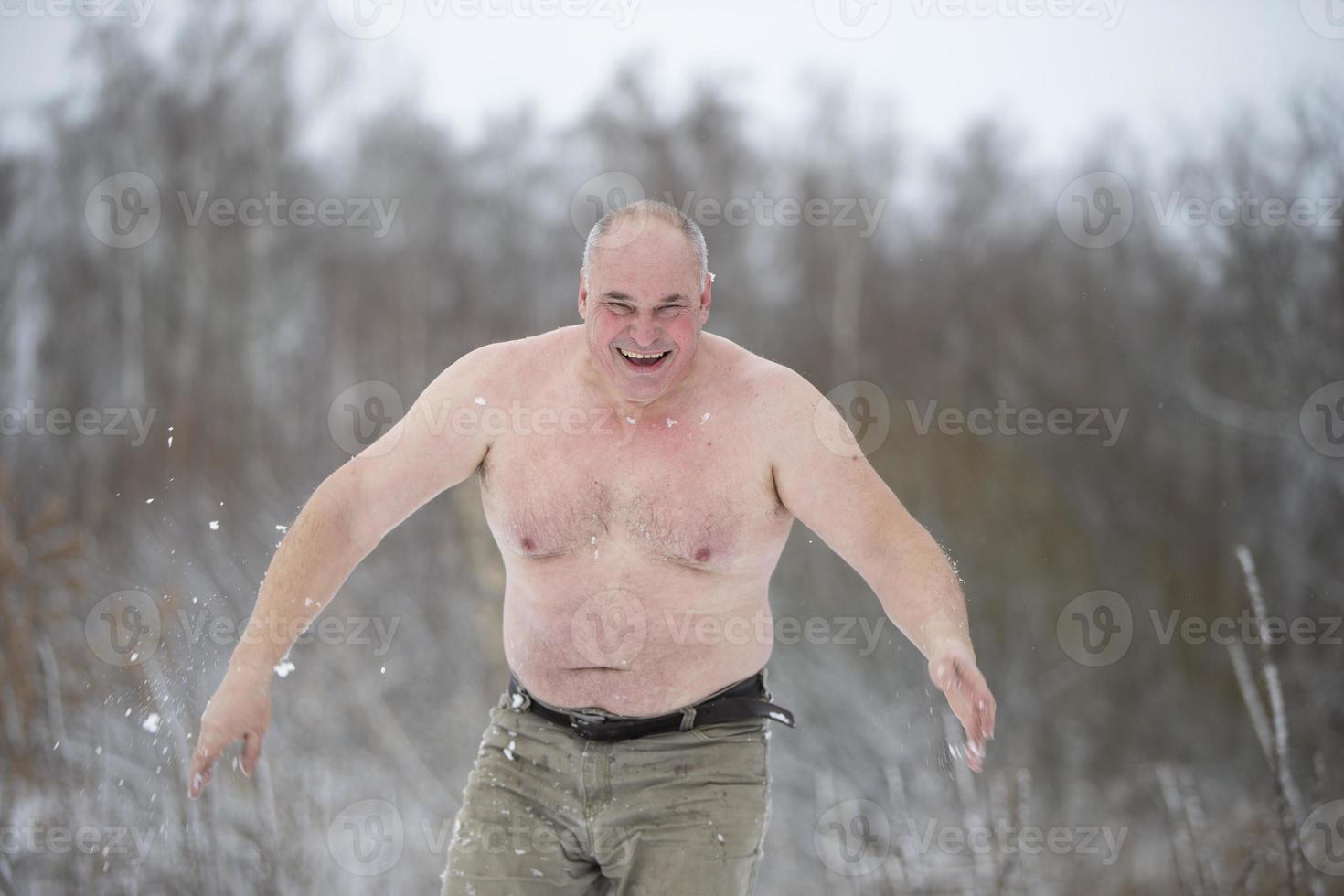 An adult man is hardened by snow on a winter day. Man with snow showers to harden his body photo