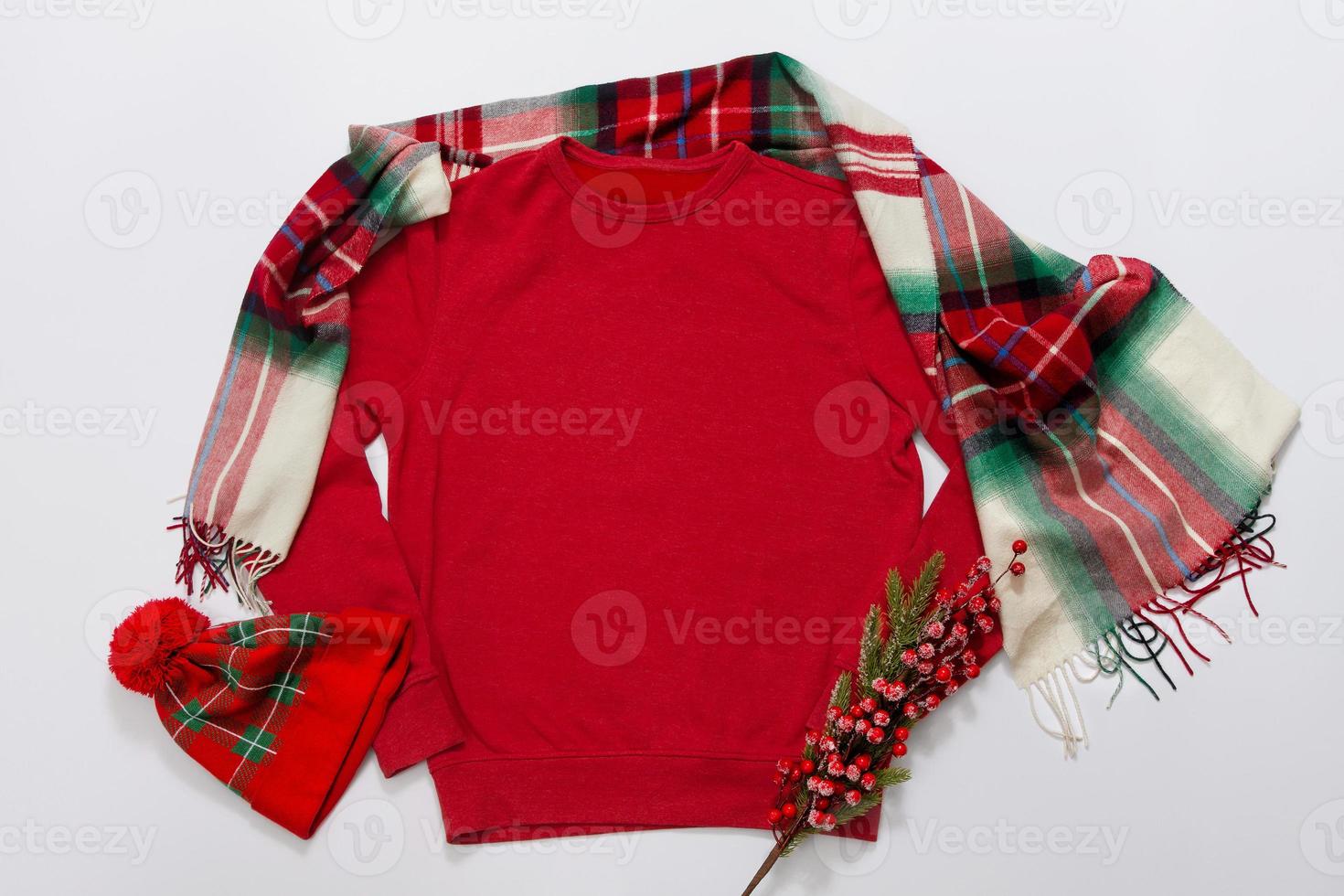 Close up red blank template sweatshirt with copy space and Christmas Holiday concept. Top view mockup hoodie and red holidays decorations on white background. Happy New Year accessories. Xmas outfit photo