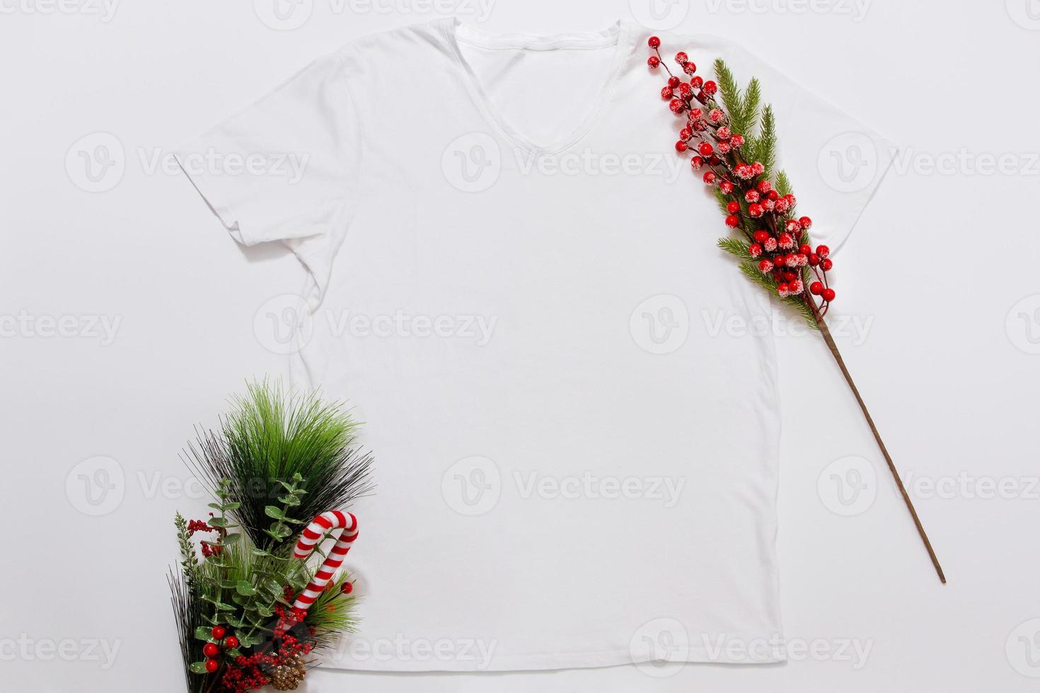 Close up white blank template t shirt with copy space and Christmas Holiday concept. Top view mockup t-shirt and red holidays decorations on white background. Happy New Year accessories. Xmas outfit photo