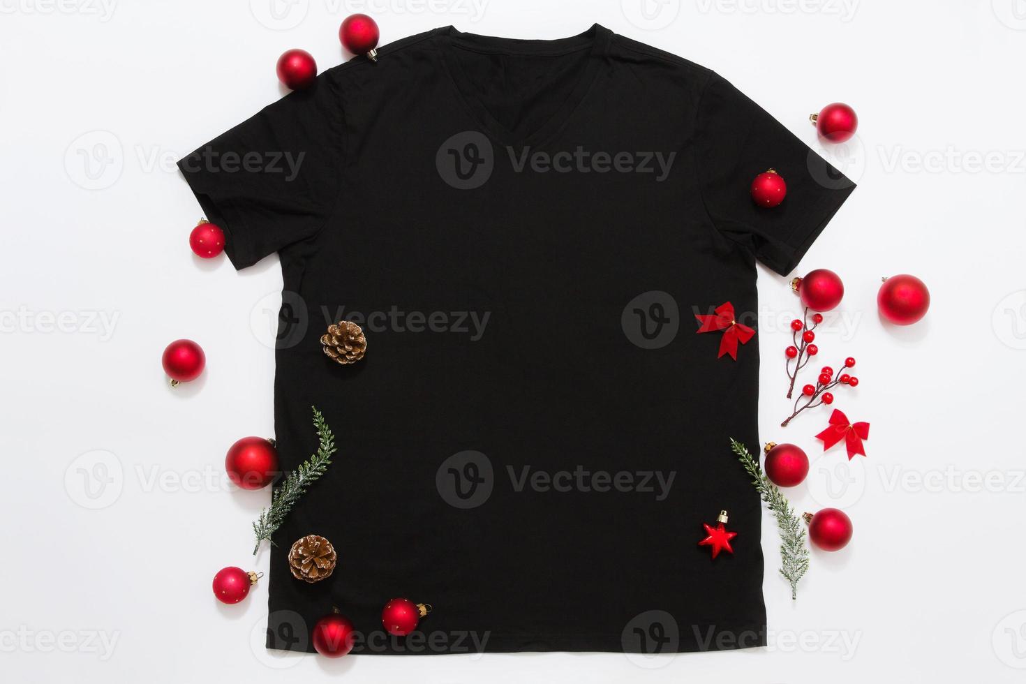 Close up black blank template t shirt with copy space and Christmas Holiday concept. Top view mockup t-shirt and red holidays decorations on white background. Happy New Year accessories. Xmas outfit photo