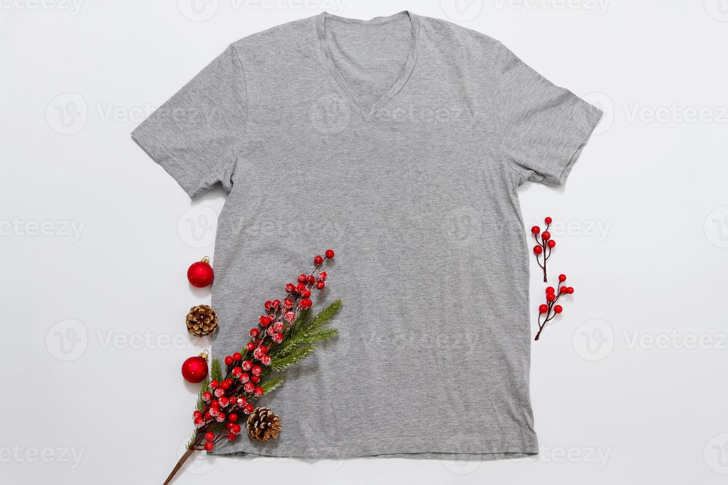 Close up grey blank template t shirt with copy space and Christmas Holiday concept. Top view mockup t-shirt and red holidays decorations on white background. Happy New Year accessories. Xmas outfit photo