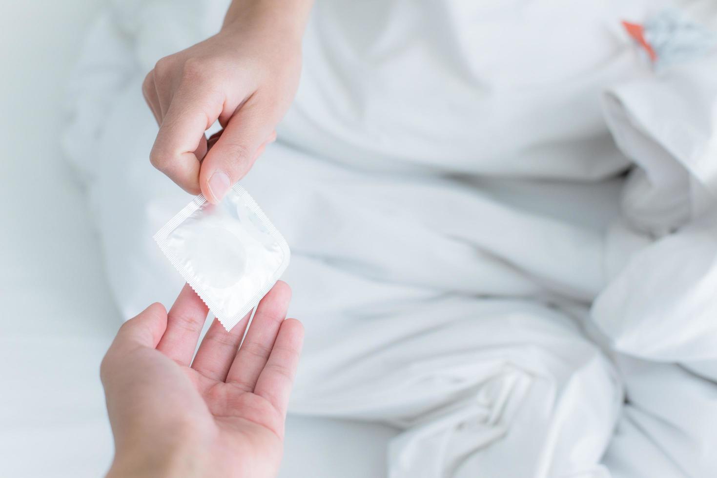 Cropped shot view of the hands of couple give the condom to the partner on bed, Save sex. photo