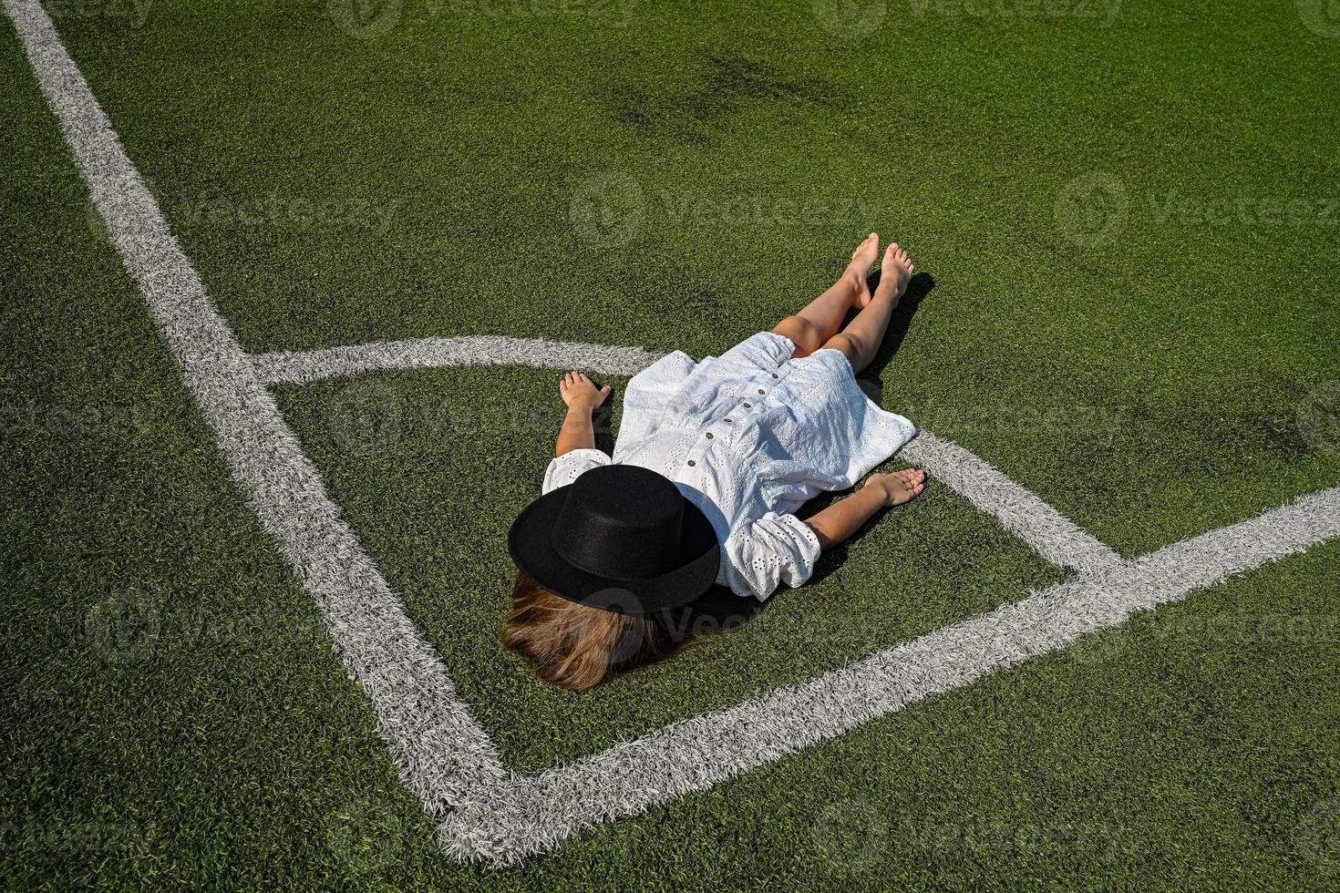 A girl is lying on a football field in a white dress. Background for the designer. photo