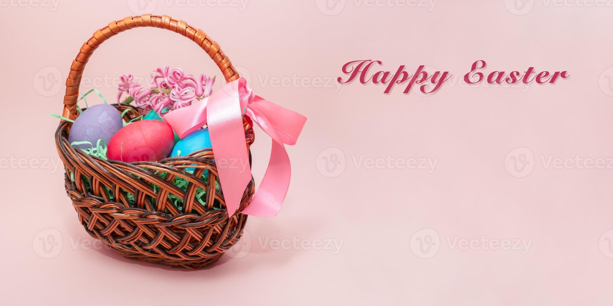 Colorful Easter eggs in wicker basket on pink background. photo