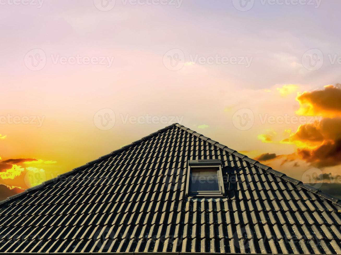 Colorful sunset. Open roof window in velux style with black roof tiles. photo