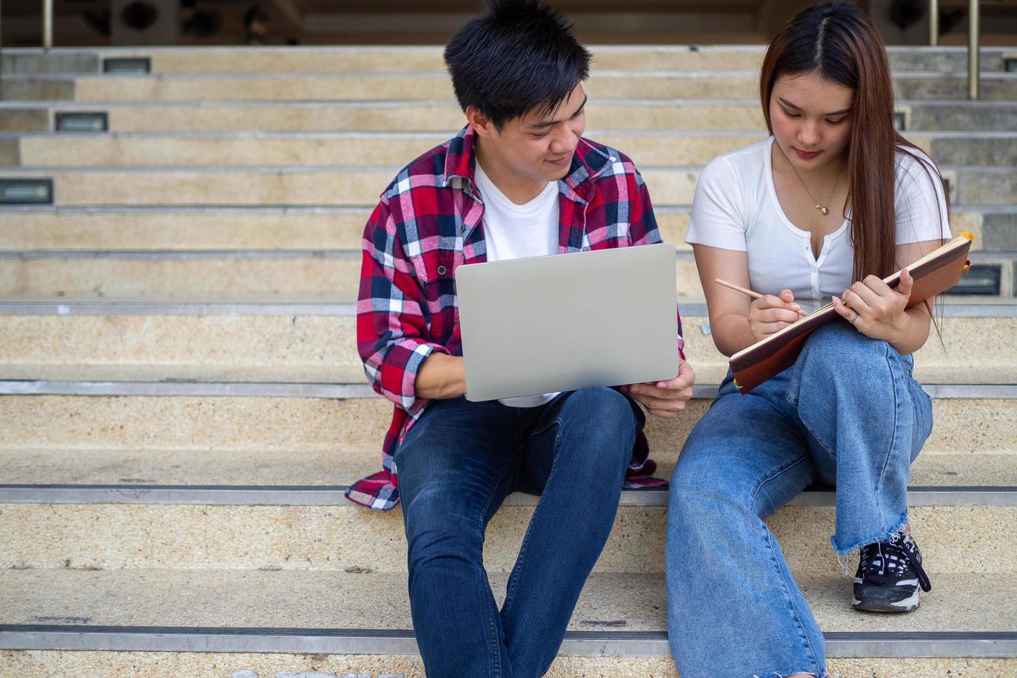 Asian male and female students sit and review the textbook, discuss the study in your free time do homework on the school grounds. photo