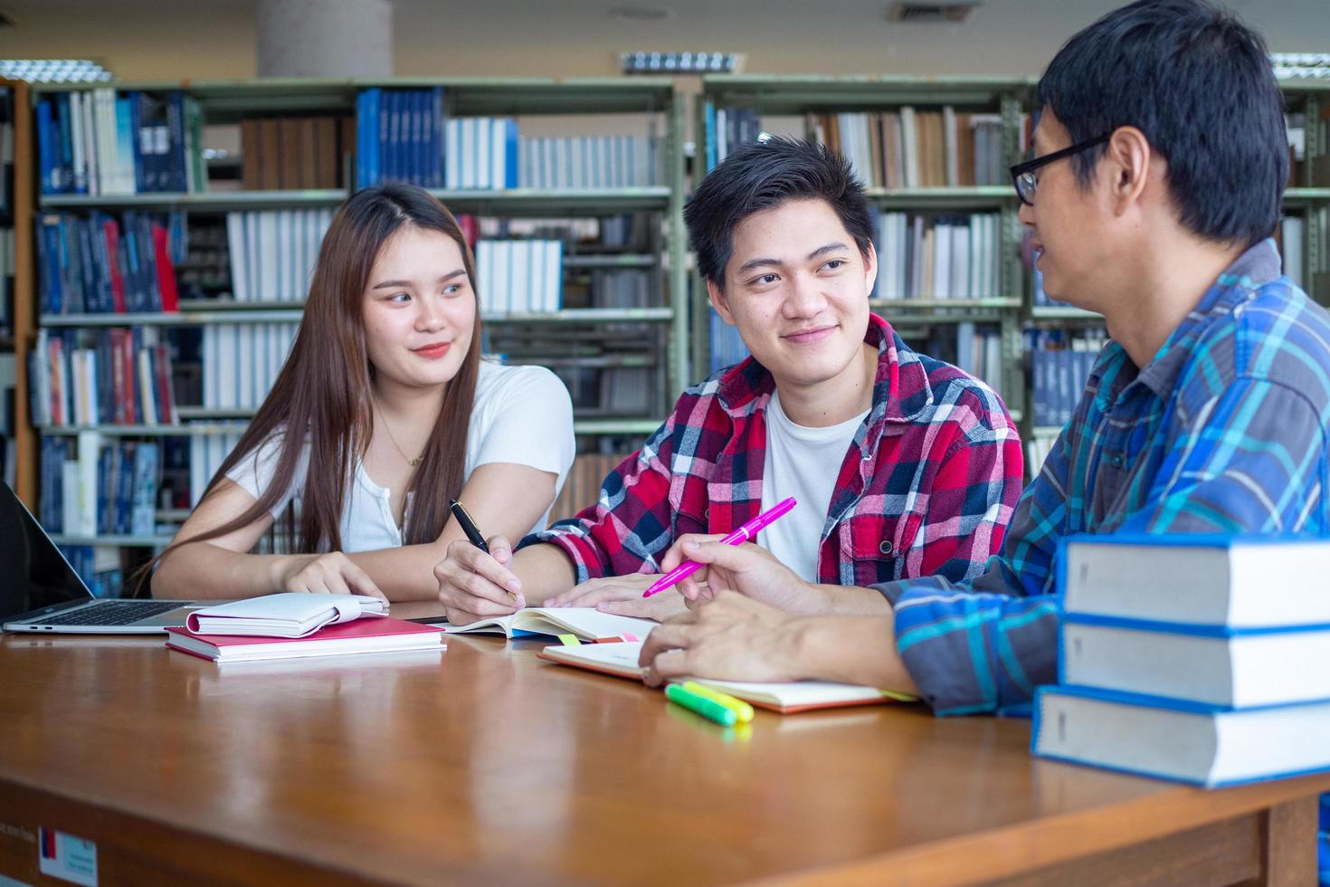 A group of Asian students sitting and discussing read books together inside the library. photo