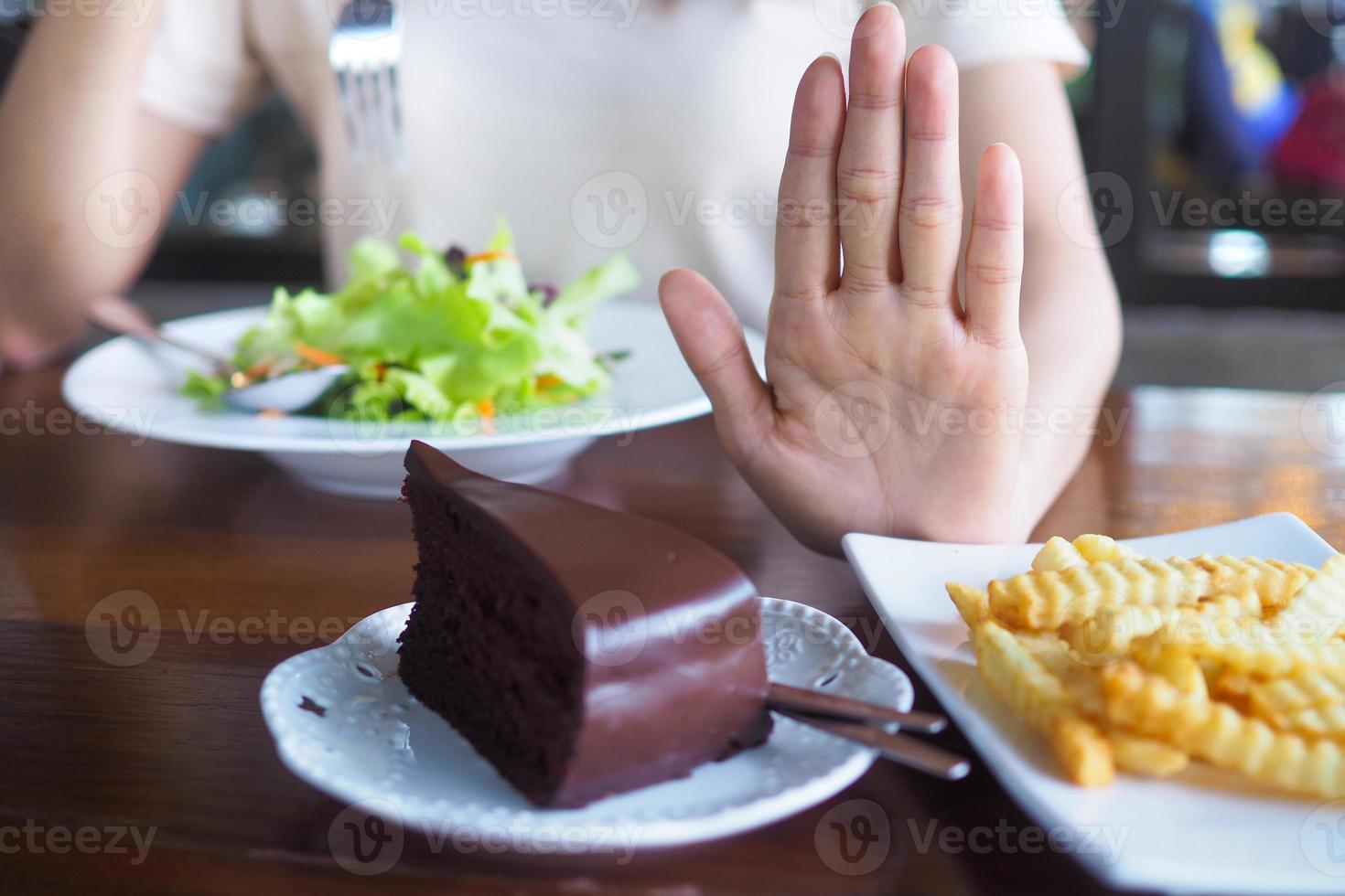 The hands of women care for health and diet, pushed from the chocolate cake and french fries plate. And choose eat vegetable or salad that contains vitamins and helps control weight for a slim stock. photo