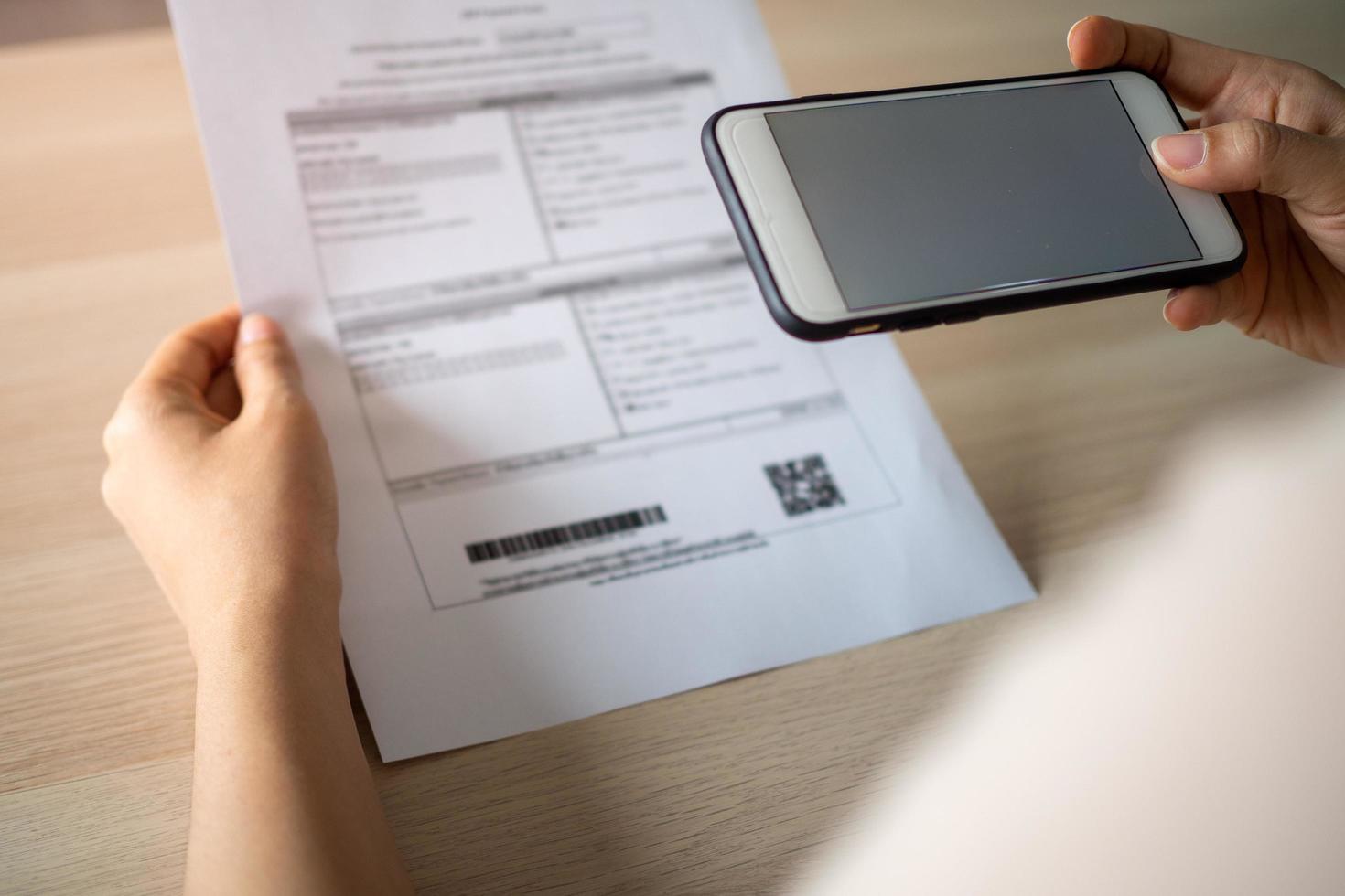 A woman uses a smartphone to scan the barcode to pay monthly phone bills after receiving an invoice sent to home. Online bill payment concept photo