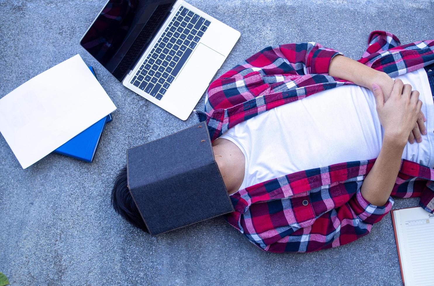 Stressed student with book cover his face. Relaxing, lazy, tired from reading exam preparation books. photo