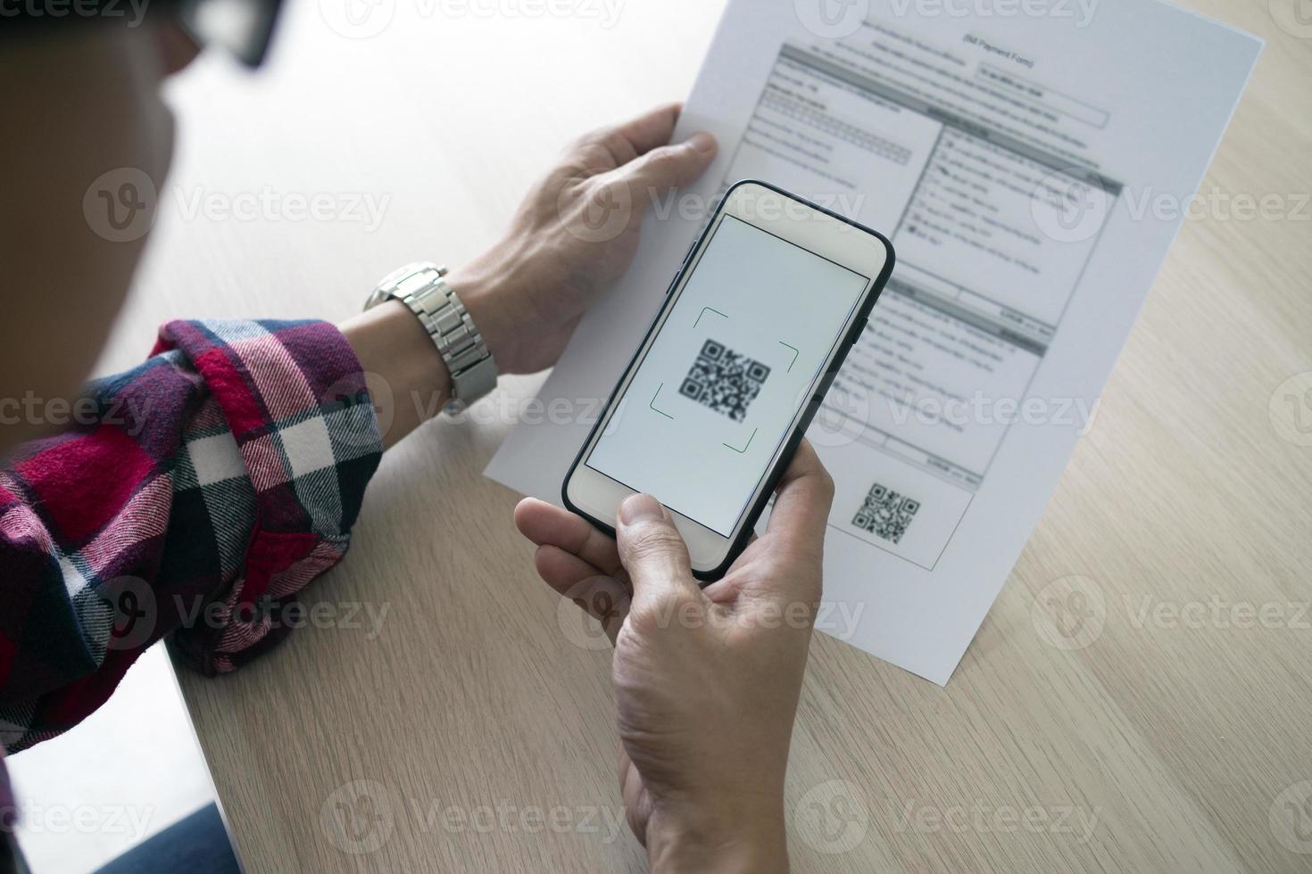 A man uses a smartphone to scan the QR code to pay monthly credit card bills after receiving an invoice sent to home. Online bill payment concept photo