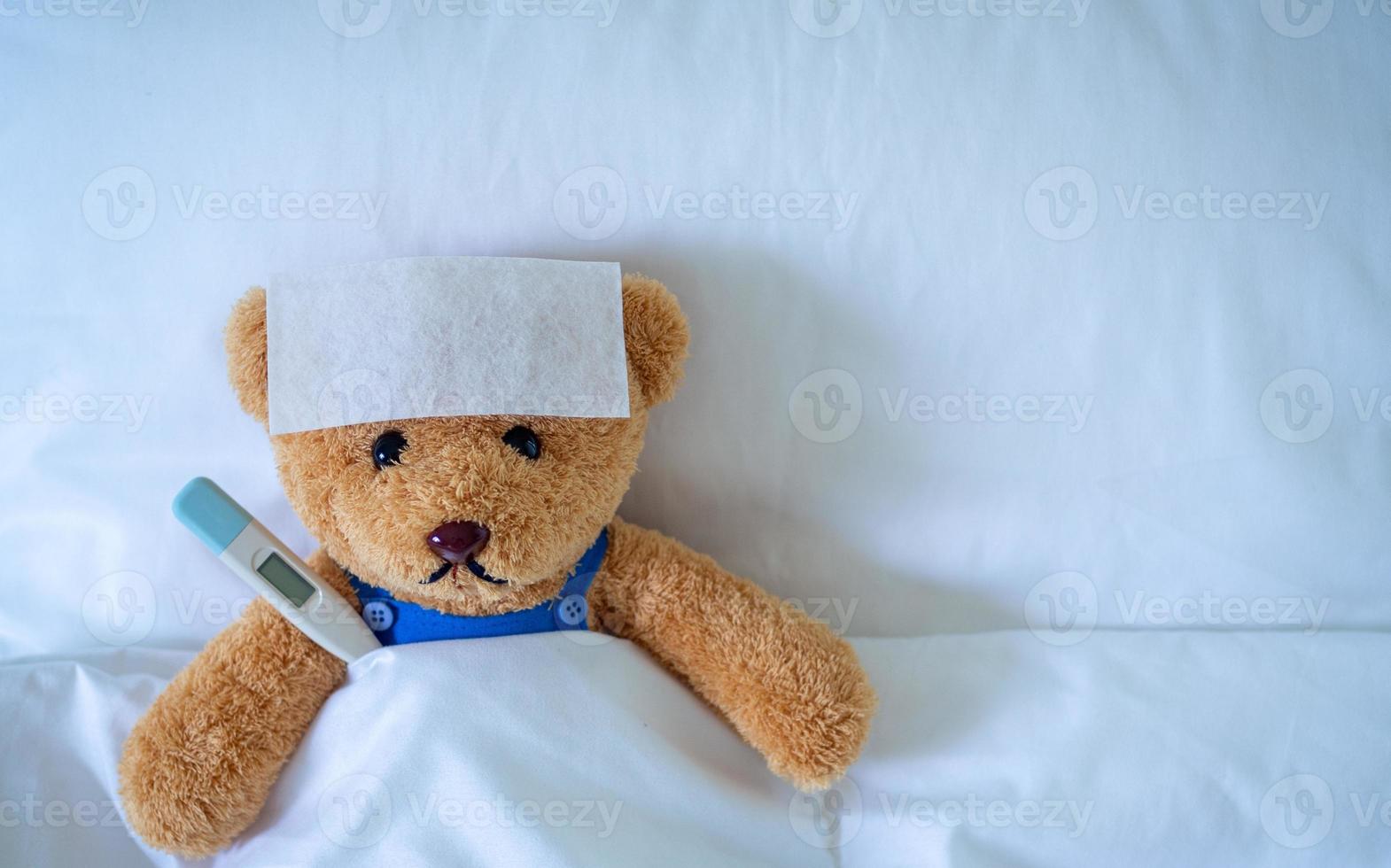 Brown teddy bear with fever reducing sheet and body temperature monitor. Used for health insurance or illness concepts photo