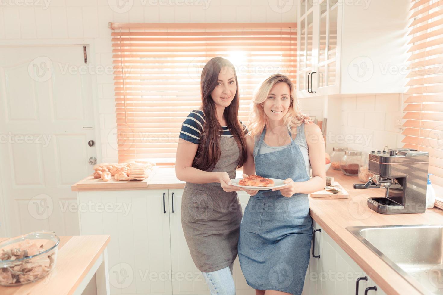 un contento joven lesbiana Pareja participación un Pizza en el cocina. el concepto de casero comida y lgbt relaciones familia y diversidad concepto. lgbt. calentar tono. foto