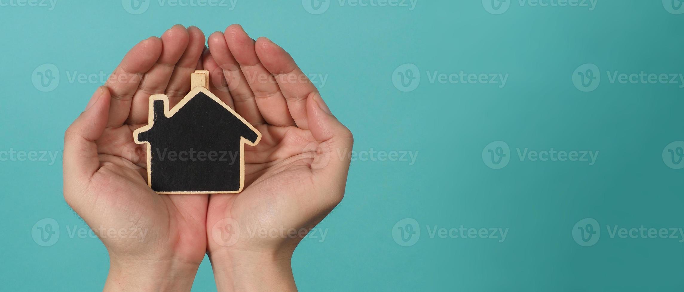 Small wood house in hands represent concepts such as home care family love real estate housing shelter insurance and mortgage. Hands holding small model house isolated on blue green studio background. photo